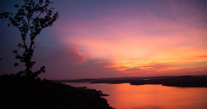 Vibrant violet, pink, orange sunset over Table Rock Lake framed by a dark shoreline landscape, Branson, MO.