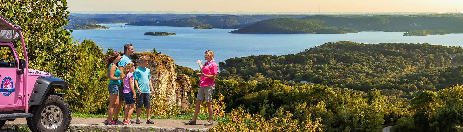 Pink® Jeep® Tour guide and guests atop Baird Mountain overlooking Table Rock Lake with Pink Jeep in foreground.