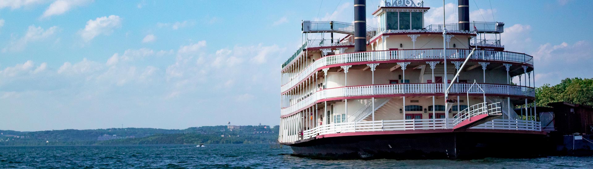 Front of the Branson Belle Showboat as it sits along the shores of Table Rock Lake, surrounded by blue waters and a summer sky.