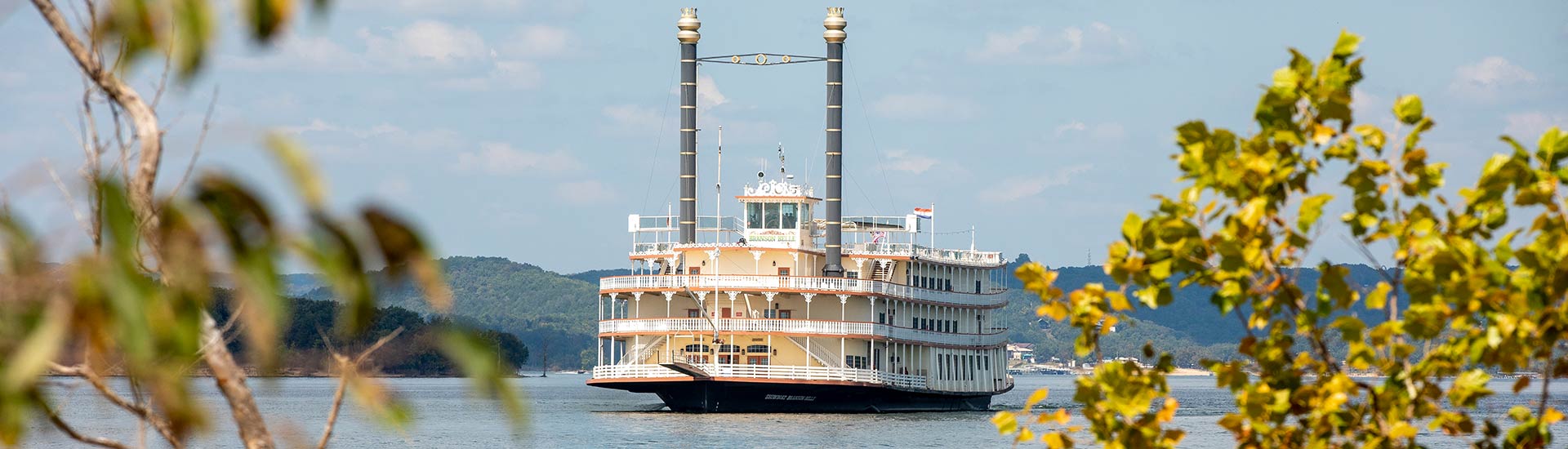 Panorama of Branson Belle Showboat on Table Rock Lake framed by trees in foreground, Branson, MO.