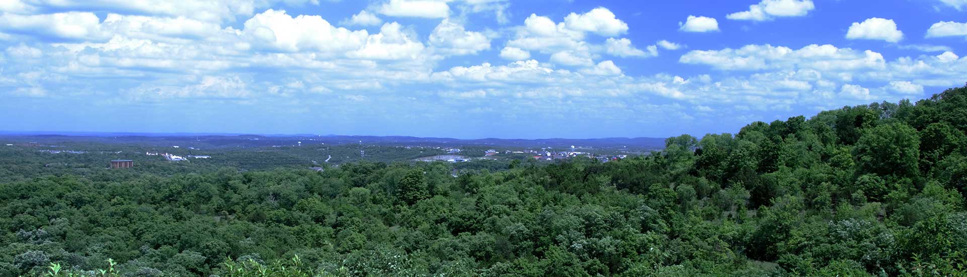 Beautiful green hillsides overlooking Branson, Missouri with puffy clouds and blue sky.