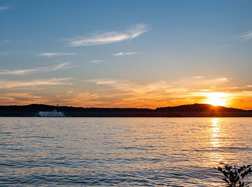 Golden sun dips below the hills behind Table Rock Lake with the Branson Belle Showboat along the shoreline.