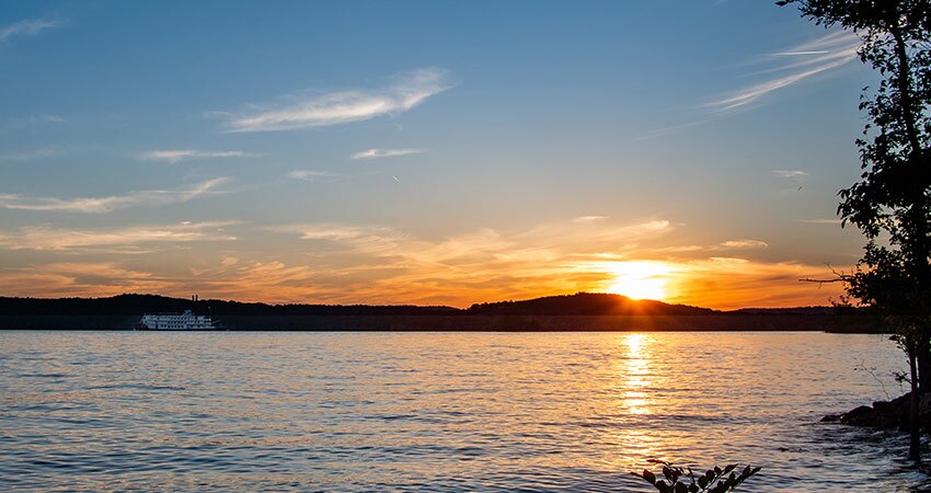 Golden sun sets behind the Branson hills at Table Rock Lake, with the Branson Belle in the distance.