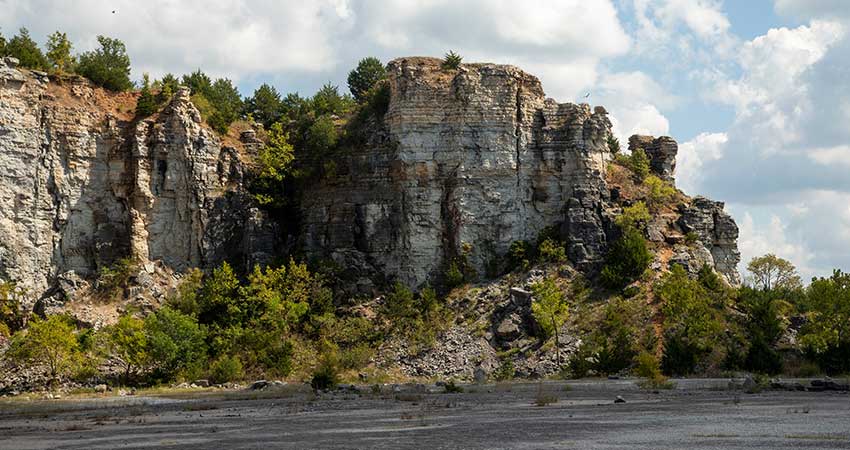 Sideview of Branson's Table Rock outcrop looking up from beach with blue sky and clouds above.