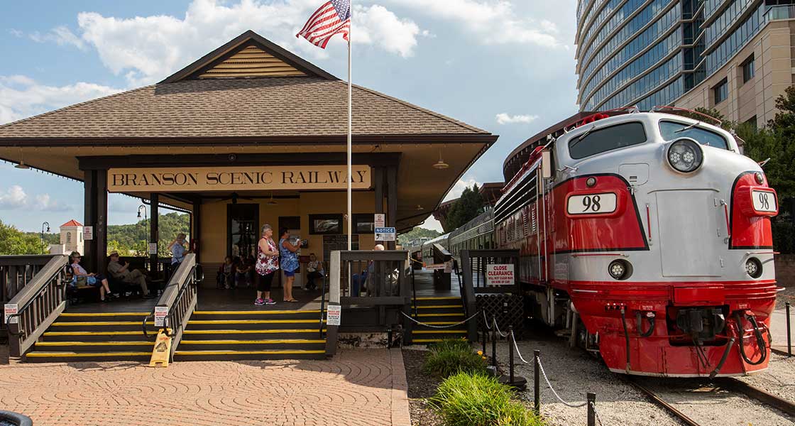 Front view of the Branson Scenic Train 98 parked next to the Branson Scenic Railway station with people on the platform.