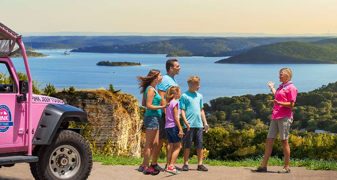 Pink® Jeep® Adventure guide and tour guests on the summit of Baird Mountain viewing Table Rock Lake, next to a Jeep® Wrangler.