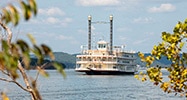 Showboat Branson Belle floating on the waters of Table Rock Lake seen through shoreline tree branches in the foreground.