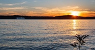 A golden sun dips below the Branson shoreline, reflecting across Table Rock Lake with the Branson Belle in the distance.