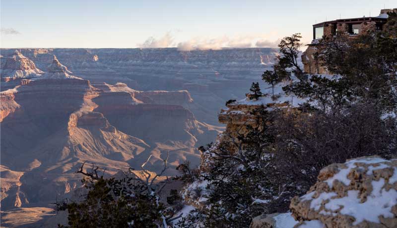 West facing view of the Grand Canyon and Yavapai Geology Museum, perched atop Yavapai Point, in the morning light with snow.