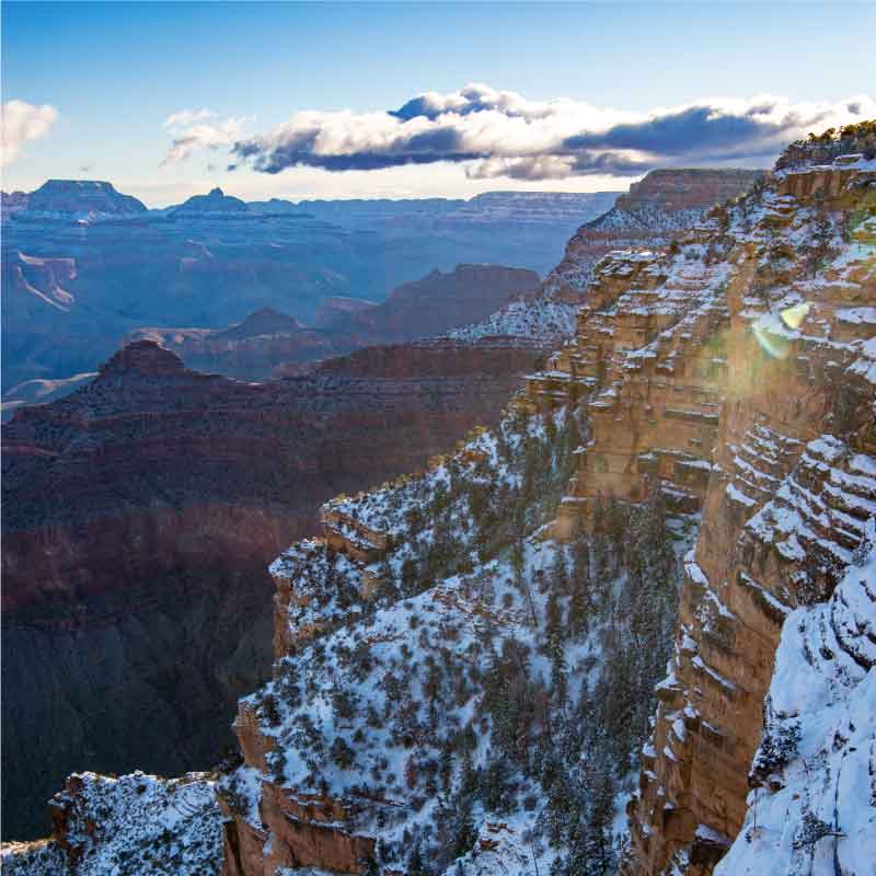 Sunlight breaks into the Grand Canyon near Yavapai Point as fresh snow clings to sandstone cliffs.