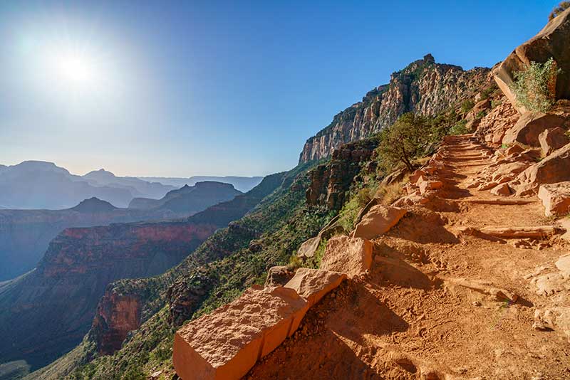 The South Kaibab Trail at Cedar Ridge in Grand Canyon National Park with the sun blazing down on canyon rims in the distance.