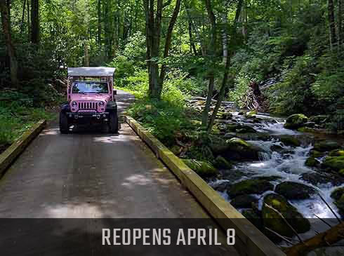Pink Jeep Wrangler on the Roaring Fork Motor Nature Trail in heavily wooded forest. Reopens April 8 banner.