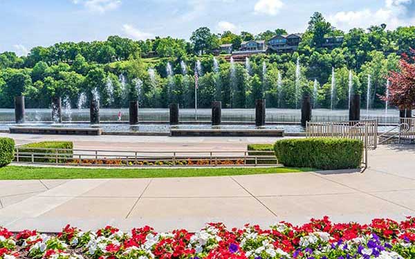 The Branson Landing Fountains erupting with water geysers along the boardwalk, framed with flowers in the foreground.