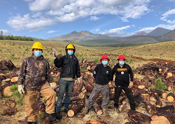 Ancestral Lands Conservation Corps team posing among cut logs in Lockett Meadow, Wood for Life Tribal Fuelwood Initiative.