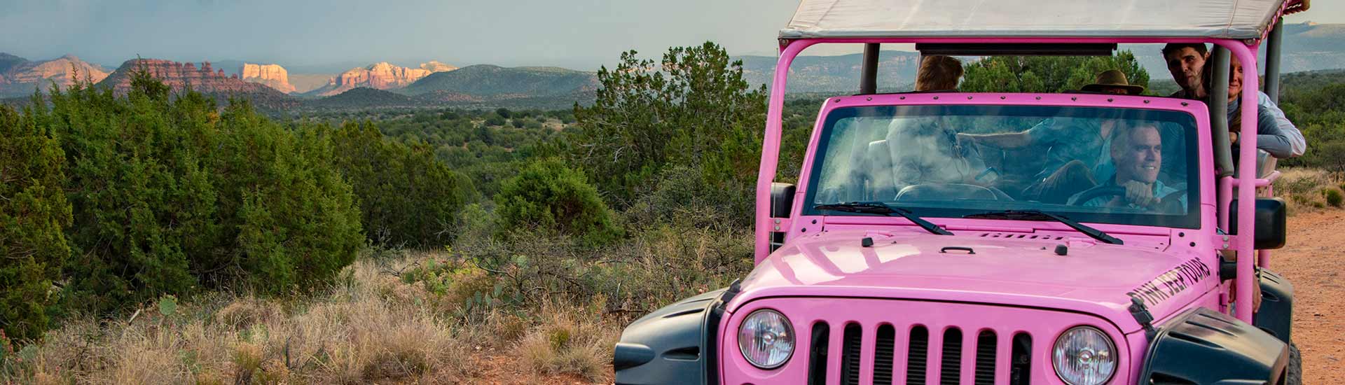 Red Rock Range tour guests in a Pink Jeep Wrangler with distance views of the red rock landscape encircling the Verde Valley.