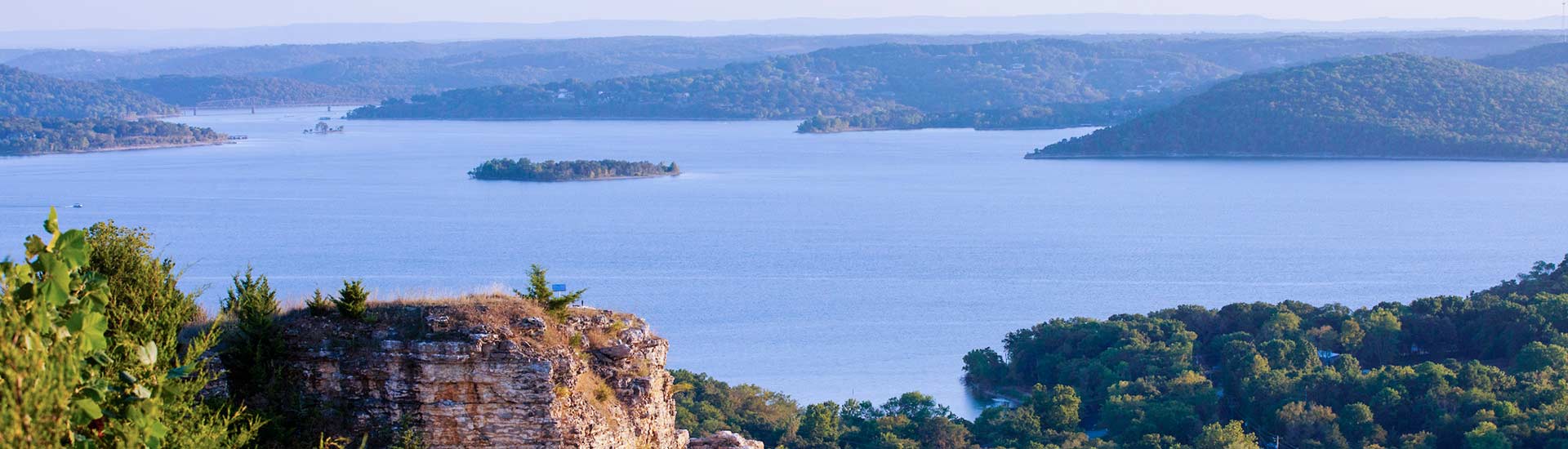 View of the blue waters and forested shorelines of Table Rock Lake from atop Baird Mountain, with cliff rock in foreground.