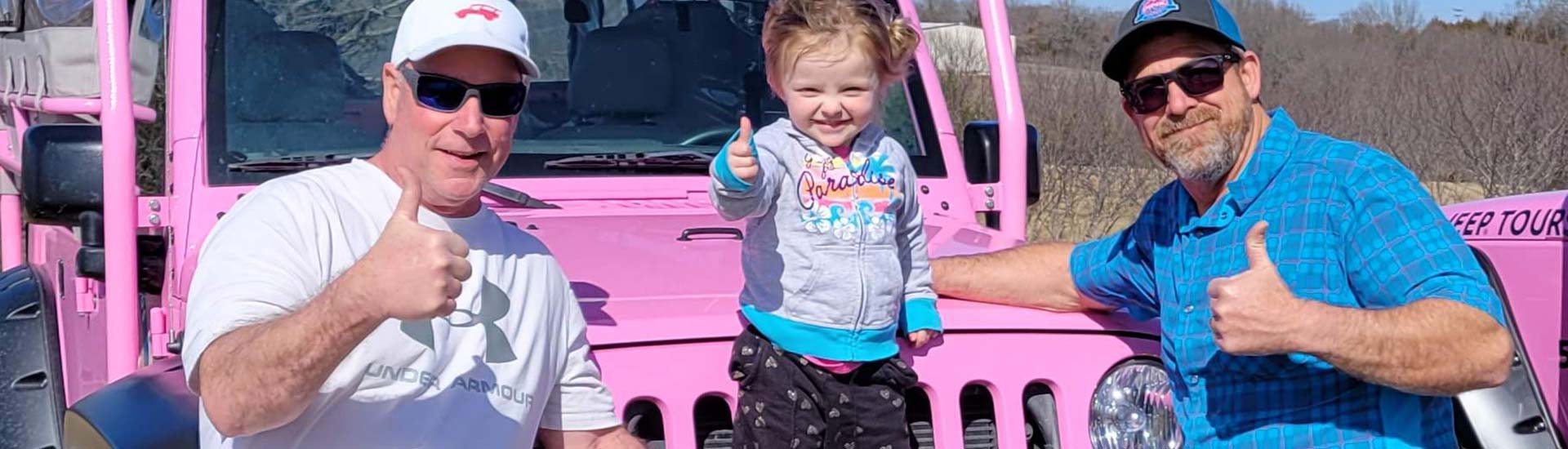 Header image of a toddler and two male adults giving a thumbs-up sign in front the grill on a Pink Jeep Wrangler.