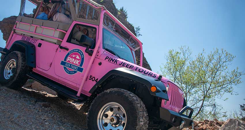 A Pink Jeep Wrangler with guests is perched atop a steep downhill slope during a Pink Jeep Branson tour.