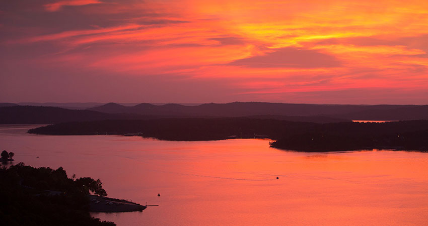 A fiery orange sunset turns Table Rock Lake crimson and casts silhouette of its shoreline during a Pink Jeep Branson Tour.