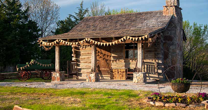 A historic, hand-hewn log cabin sits atop Baird Mountain lit by the warm afternoon sun, visit with Pink Jeep Tours Branson.