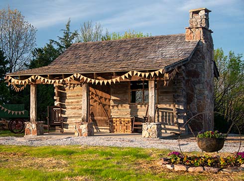 A restored hand-hewn cabin sits atop Baird Mountain aglow in the afternoon sun, visit with Pink Jeep Tours Branson.