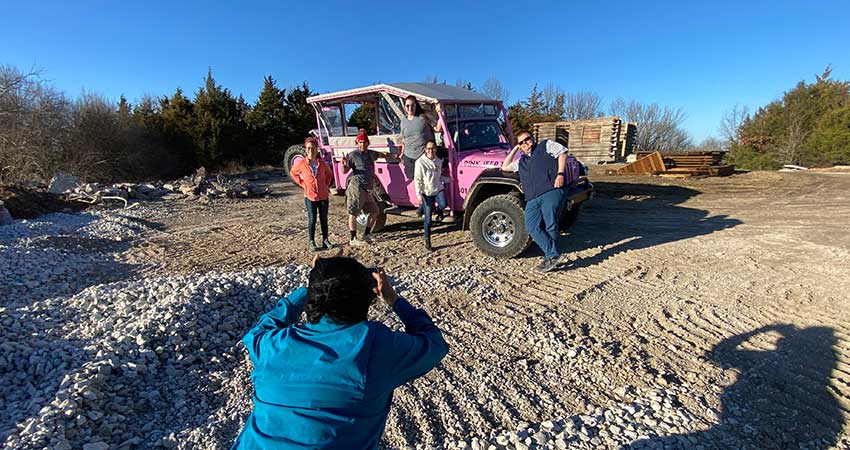 Pink Jeep Branson tour guide taking a photo of five people posing on a Jeep Wrangle atop Baird Mountain in the afternoon sun.