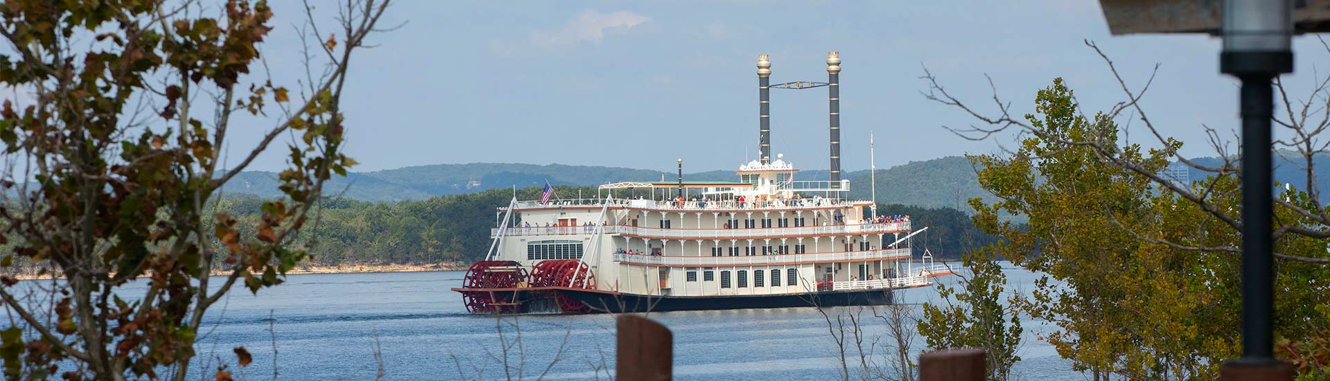 The Showboat Branson Belle framed by trees as it glides across Table Rock Lake with its paddle wheel in motion.