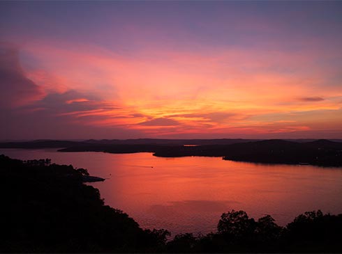 A violet-orange sunset turns the sky and Table Rock Lake crimson in Branson, Missouri at twilight.