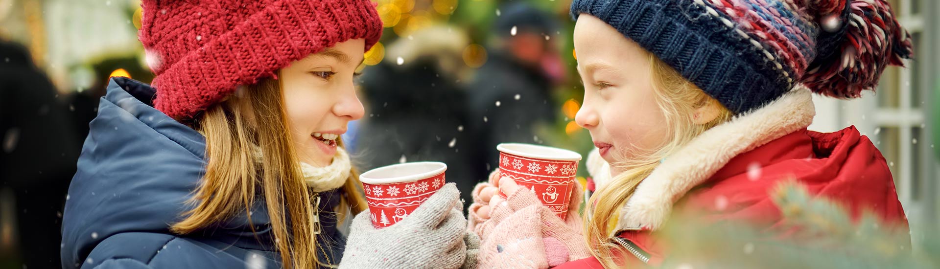 Close-up of two young girls drinking warm wassail outside at Christmastime among falling snowflakes, Branson, MO.