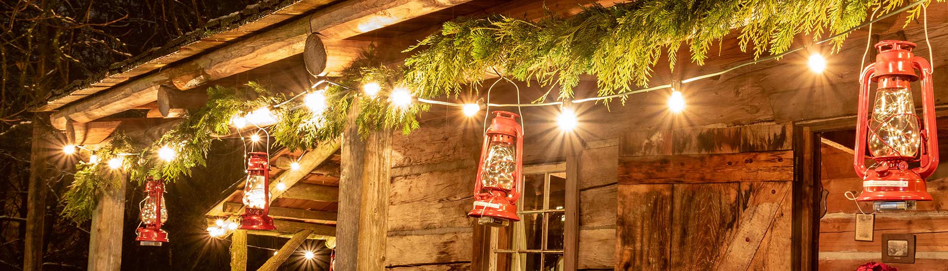 Header image of Christmas garland, twinkle lights and red lanterns hanging from a log cabin porch roof, Pink Jeep Tours Branson Christmas Tour.