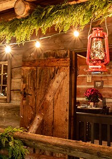 Open doorway of a rough-hewn log cabin porch with a Christmas poinsettia on table inside, Christmastime in Branson, Missouri with Pink Jeep Tours.