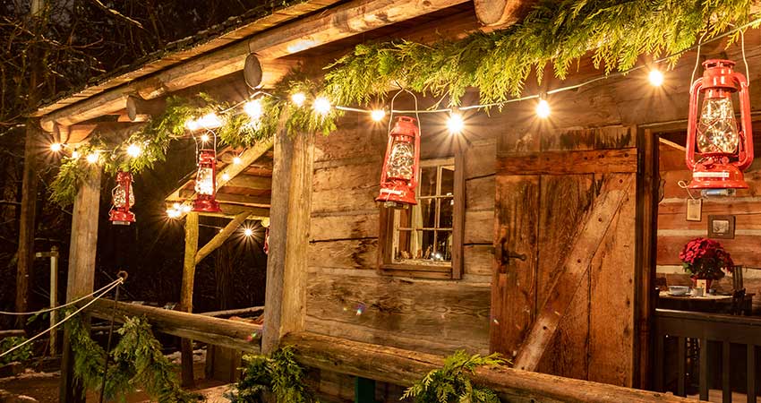 Rough-hewn log cabin porch brightly lit with Christmas garland, twinkle lights and red lanterns in Branson, MO.