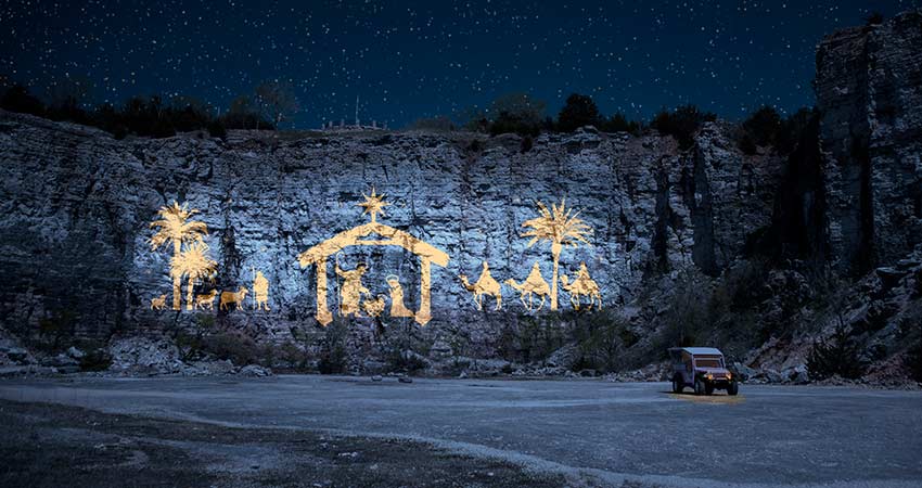Tallest nativity scene in Branson, MO illuminated against the cliff face of Baird Mountain at night, with Pink Jeep Wrangler in foreground.