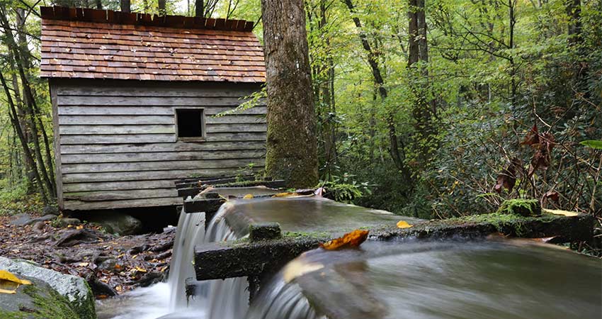 Historic grist mill along the Roaring Fork Motor Nature Trail near Gatlinburg, Tenneesee with water roaring over its shute in the foreground.