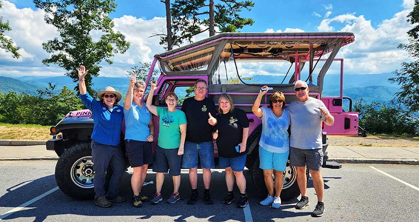 Family and tour guide posing in front of a Pink Jeep Wrangler with Smoky Mountain hilltops in background, Foothills Parkway Tour.