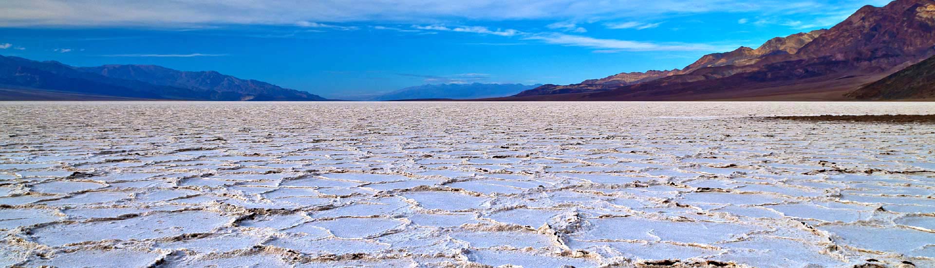  White salt flats at Death Valley National Park with mountain range and blue sky in the distance.