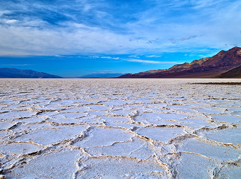 Closeup of white salt flats at Death Valley National Park with mountains and blue sky in the distance.