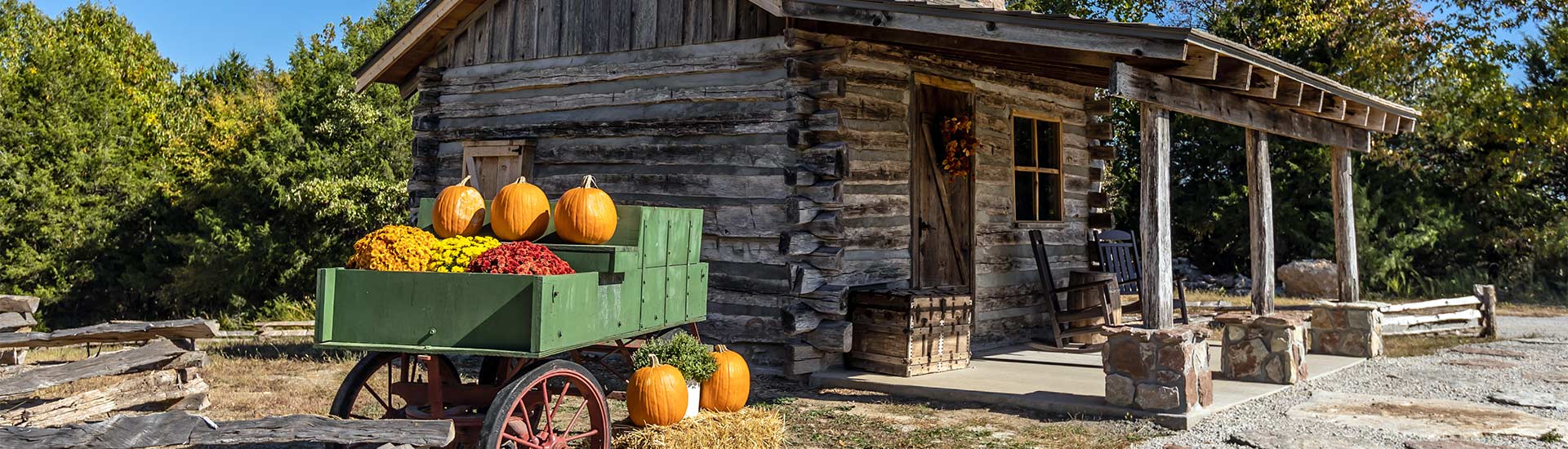 Header image of historic log cabin with pumpkin wagon in foreground, visit with Pink Jeep Tours Branson, Missouri.