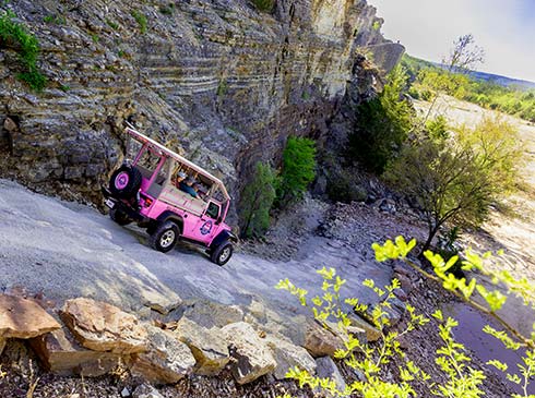 A Pink Jeep Wrangler navigates down a steep off-road trail beside the rockface of Baird Mountain into the quarry below.