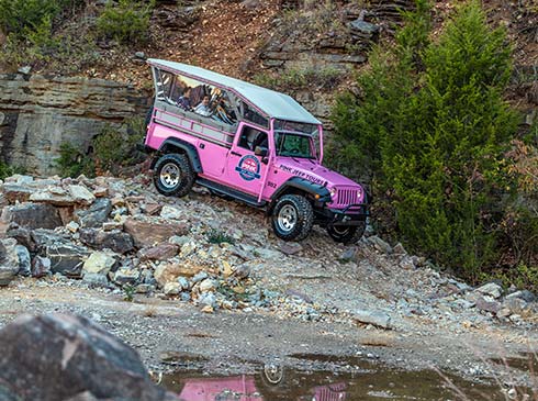 Pink Jeep Wrangler perched on a rocky slope next to the rockface of Baird Mountain, with its image reflected in a pond below.