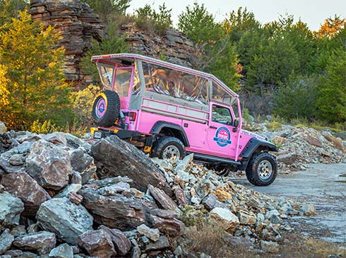 Pink Jeep entering rock quarry with warm glow of late afternoon sun against trees, Pink Jeep Branson Tour.