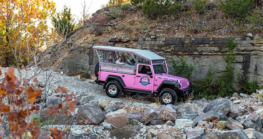 Pink Jeep Wrangler with tour guests traveling down a rocky, 4x4 trail on Baird Mountain, with autumn leaves in the foreground.