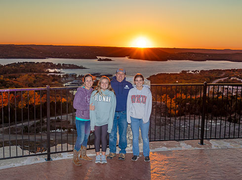 Family posing in front of Table Rock lake during a vibrant orange sunset, Baird Mountain Overlook, Pink Jeep Tours Branson.