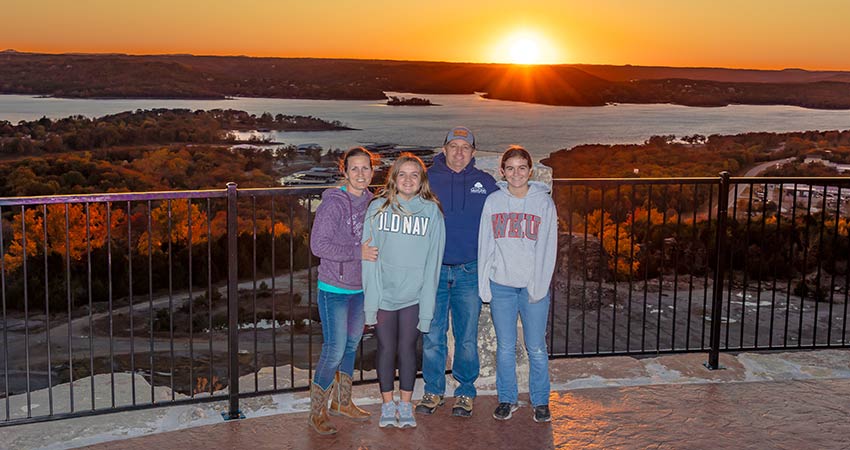 Family posing in front of Table Rock Lake with vibrant range sunset, Pink Jeep Tours Branson Baird Mountain lookout.