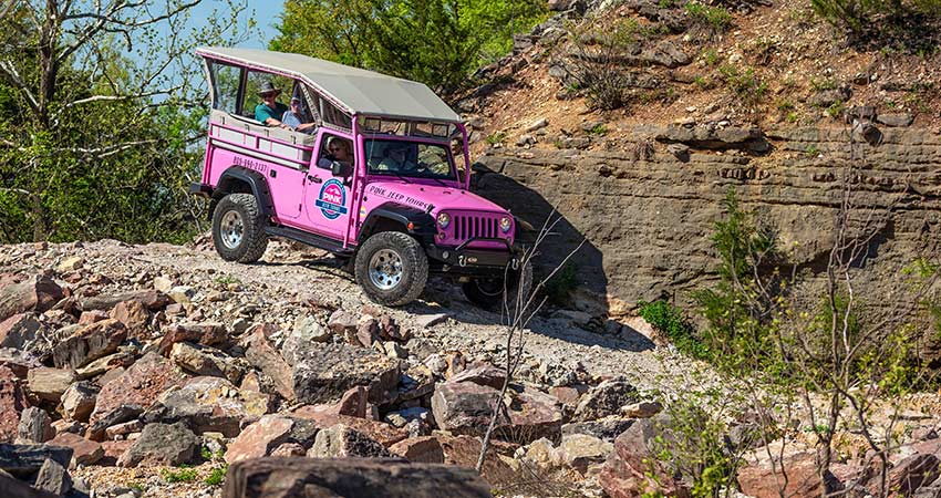 A Pink Jeep Wrangler with guests rounds a cliff side corner down a 4x4 trail on Baird Mountain, Pink Jeep Tours Branson.