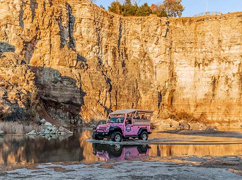 A Pink Jeep Wrangler glides through still waters below the golden rockface of Baird Mountain and its private lookout above.