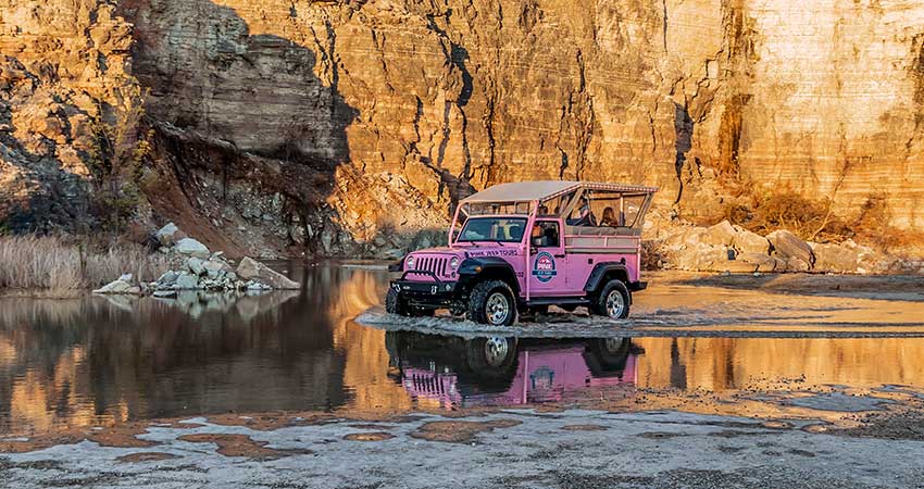 A Pink Jeep Wrangler glides through water below the cliff face of Baird Mountain lit by a golden sunset, Pink Jeep Tours Branson.