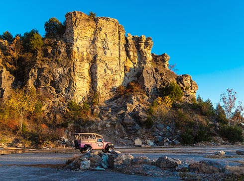 A Pink Jeep Tour crosses the cliff face of Baird Mountain along the rock quarry floor at sunset, Pink Jeep Tours, Branson.