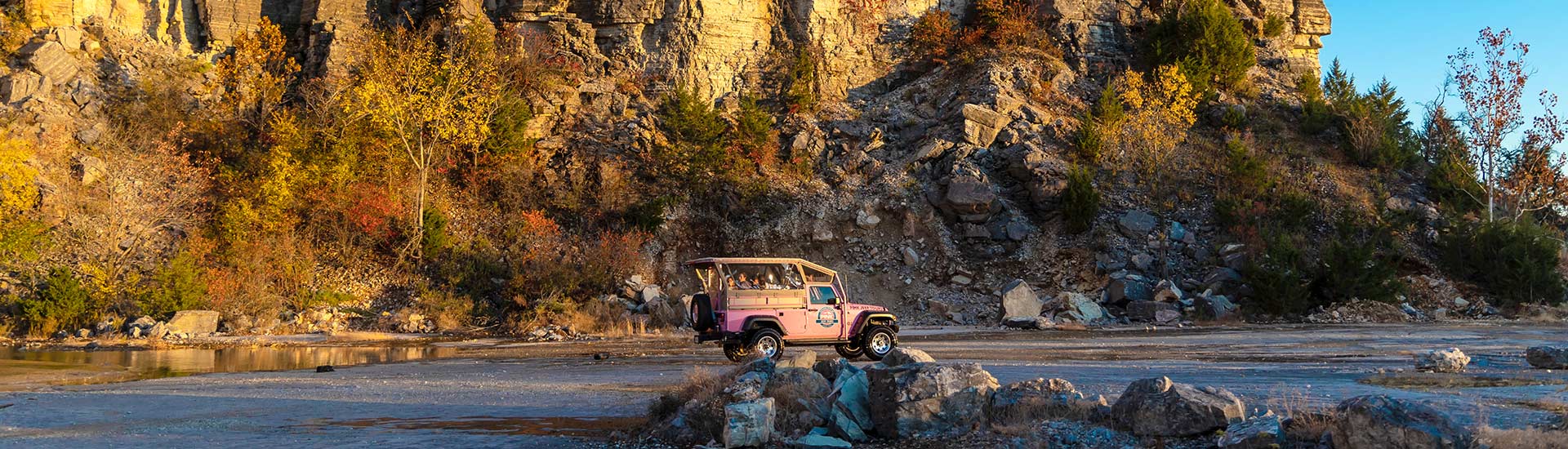 Header image of Pink Jeep Wrangler on tour crossing the rock quarry floor below the golden-lit rockface of Baird Mountain.