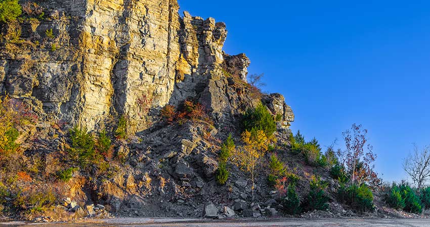 Autumn trees are scattered along the base of Baird Mountains’ cliff side, lit by a golden sunlight against a deep blue sky.